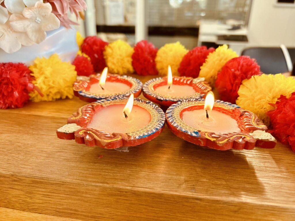 Four small Diyas on a table with red and yellow flowers
